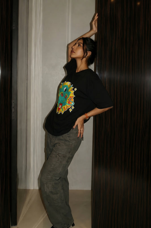 Person wearing a black t-shirt with a colorful embroidery design, standing against a dark background.