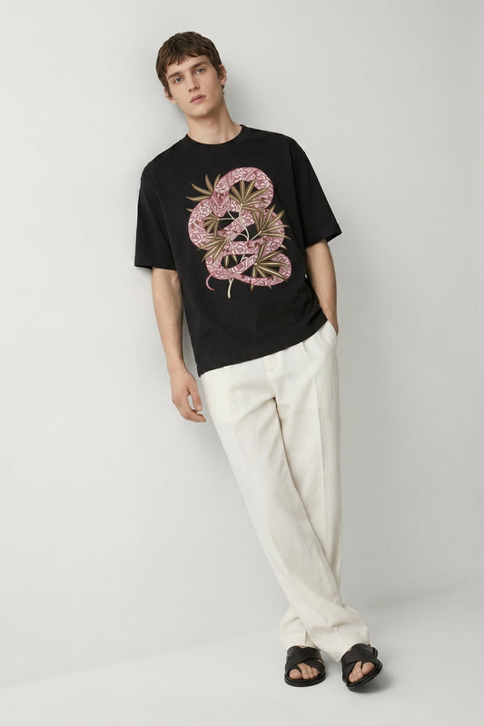 Man wearing a black t-shirt with a pink and gold graphic design and white pants on a light gray background