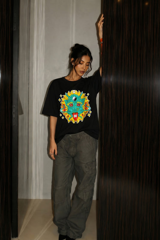 Person wearing a black t-shirt with a colorful embroidery design, standing in a room.
