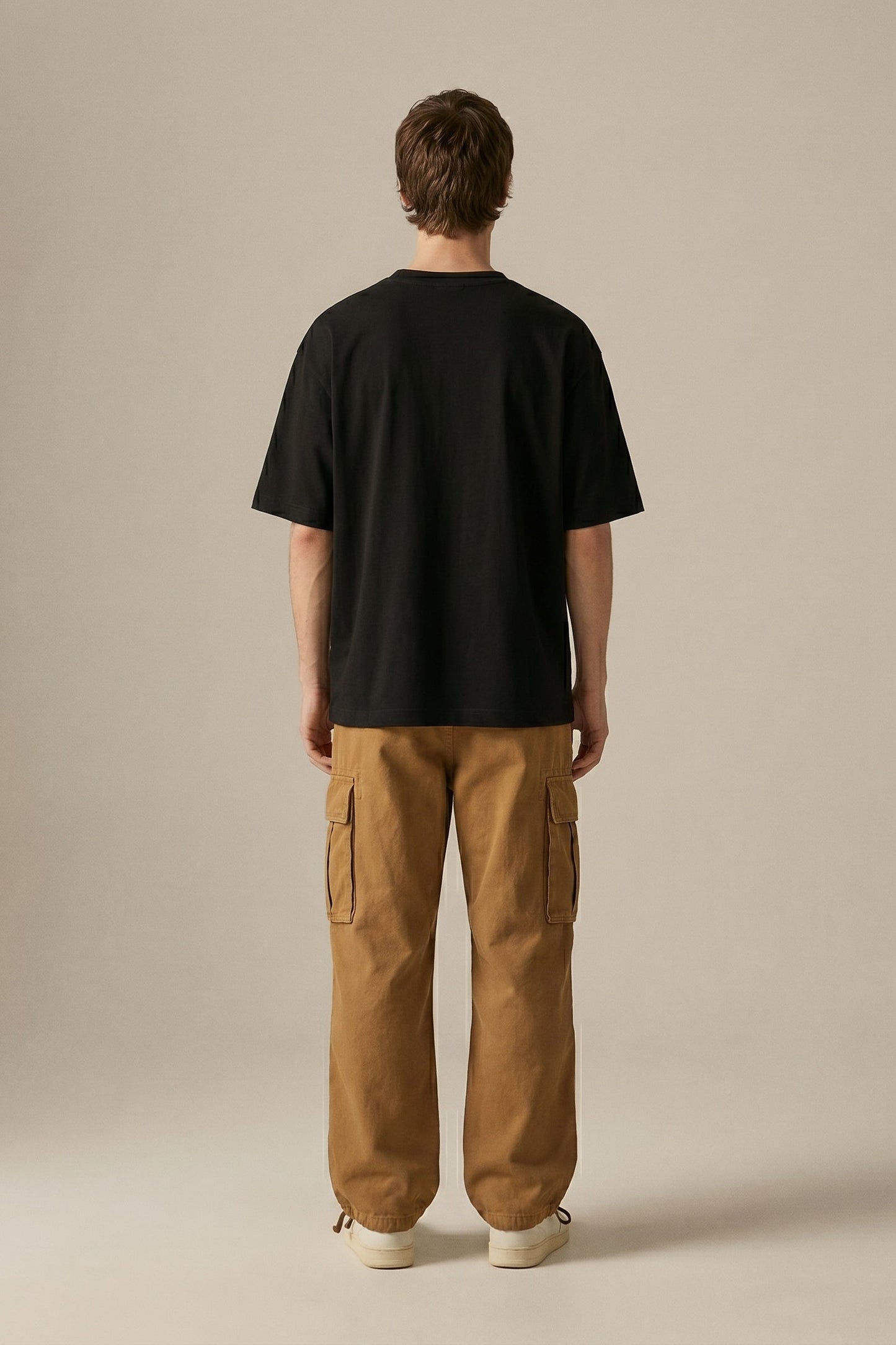 Person wearing a black t-shirt and brown cargo pants on a beige background
