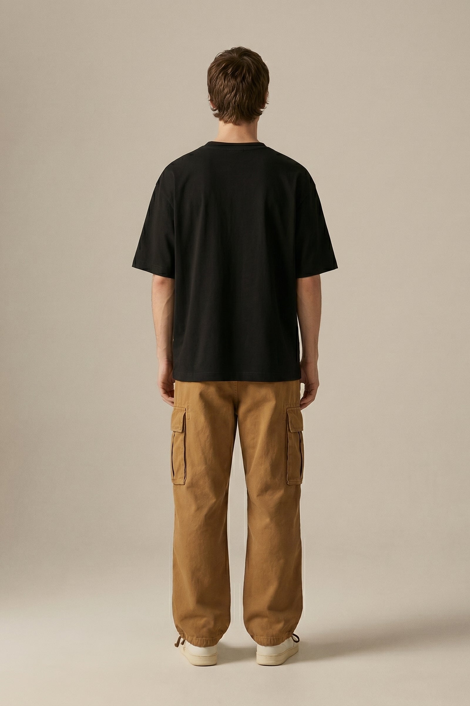 Person wearing a black t-shirt and brown cargo pants on a beige background