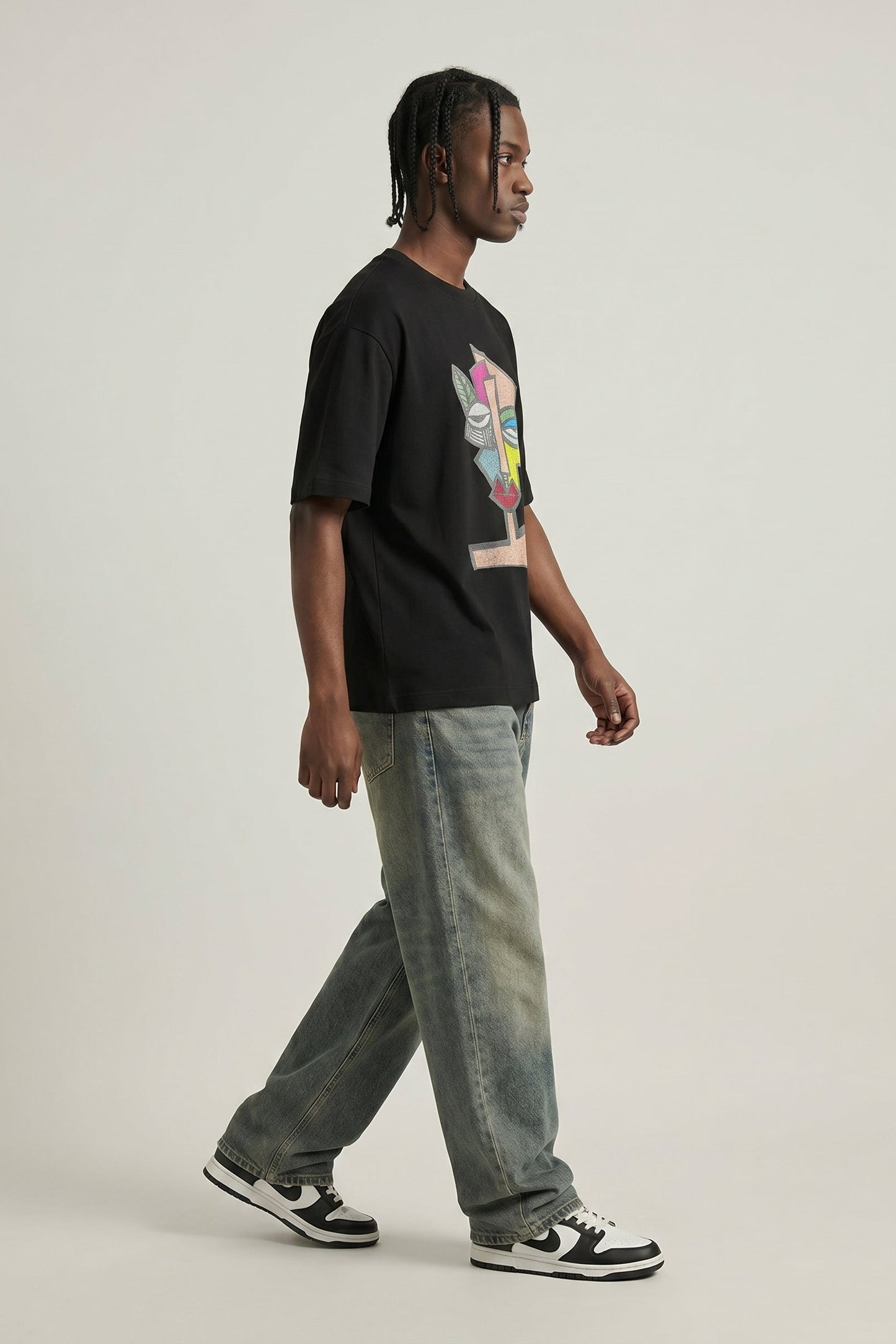 Person wearing a black t-shirt with a colorful graphic and light blue jeans on a plain background