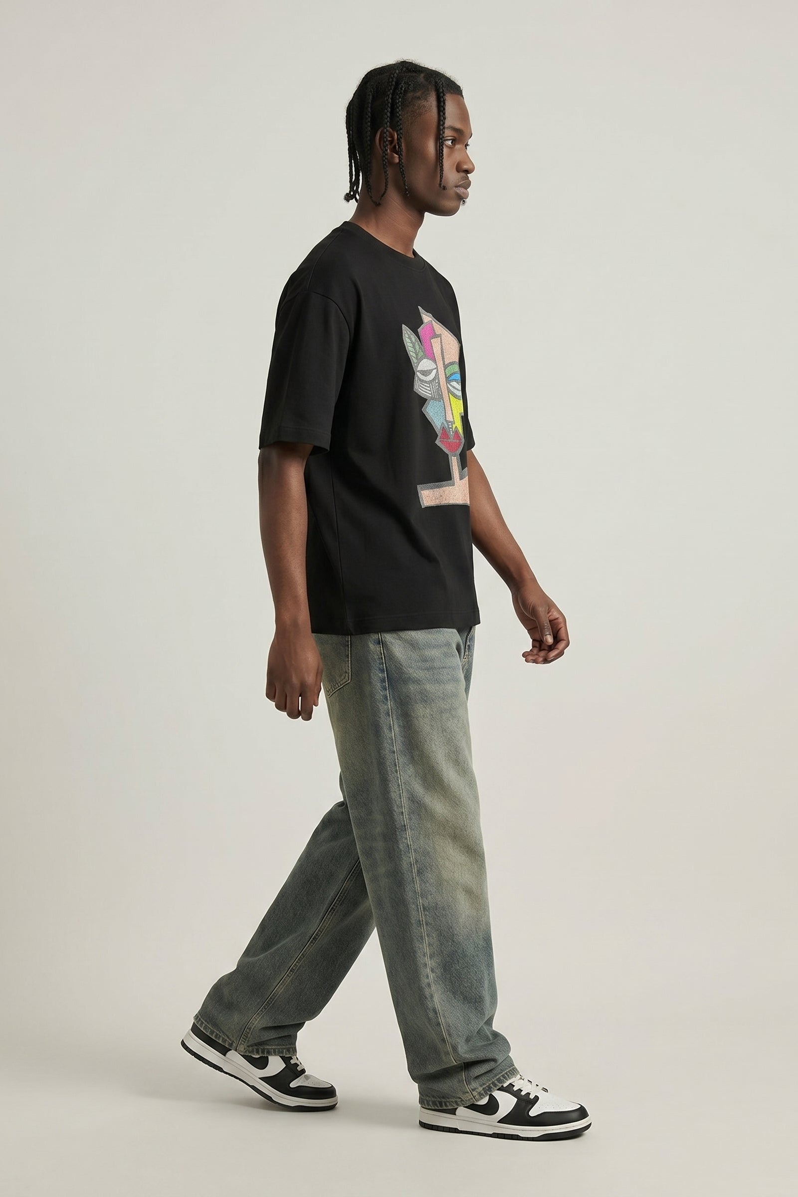 Person wearing a black t-shirt with a colorful graphic and light blue jeans on a plain background