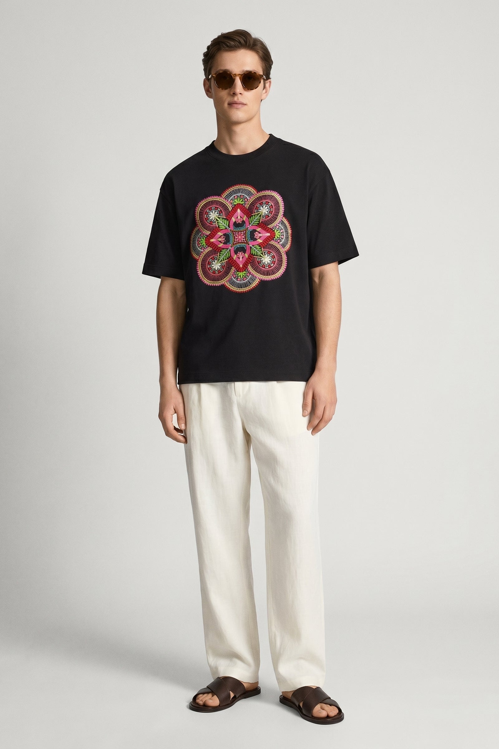 Man wearing a black t-shirt with a colorful geometric design and white pants on a light gray background