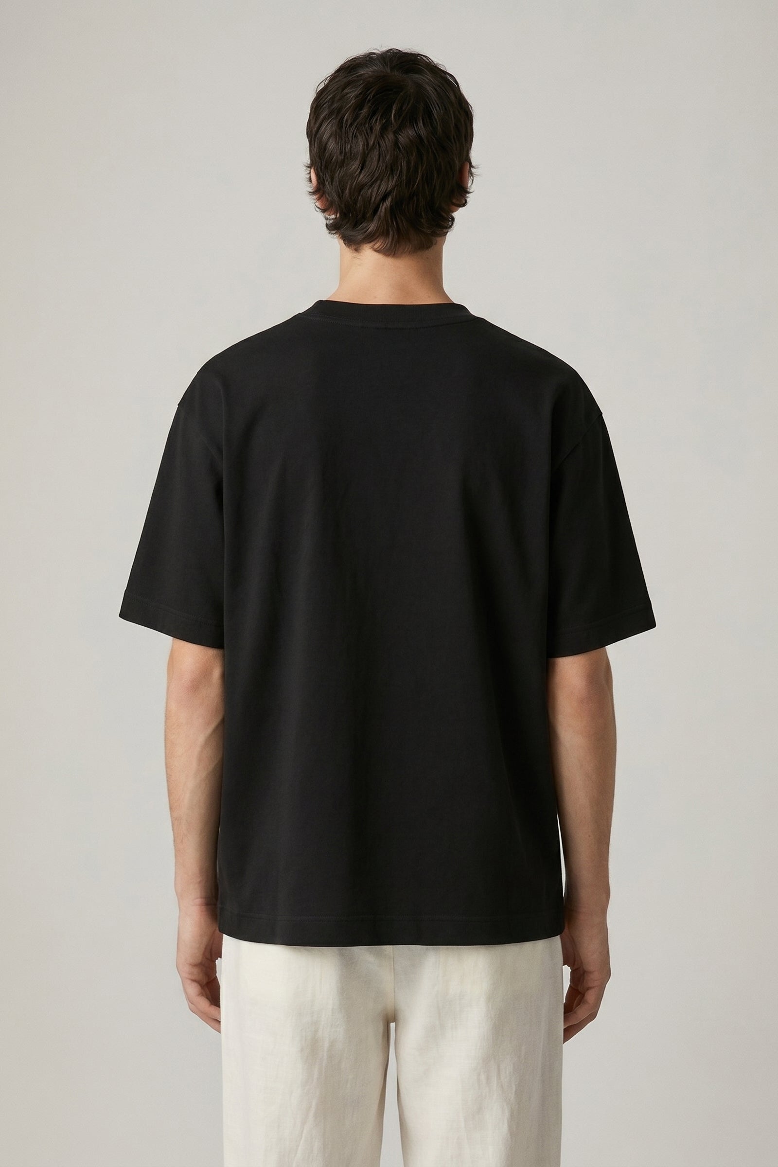 Person wearing a black t-shirt and light-colored pants on a plain background
