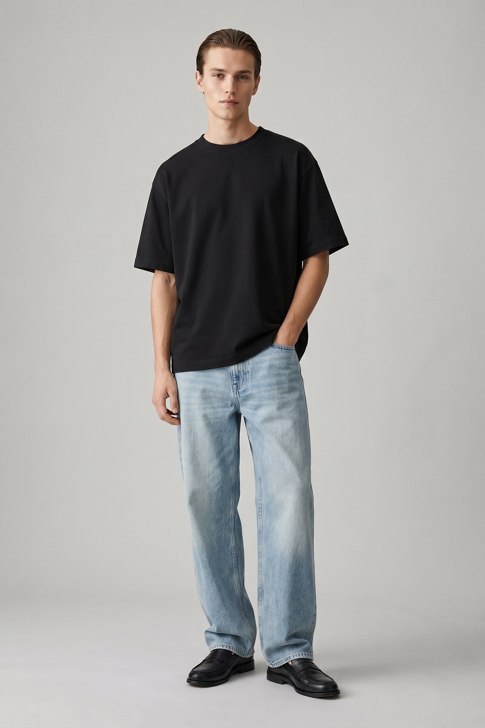 Man wearing a black t-shirt and light blue jeans on a gray background