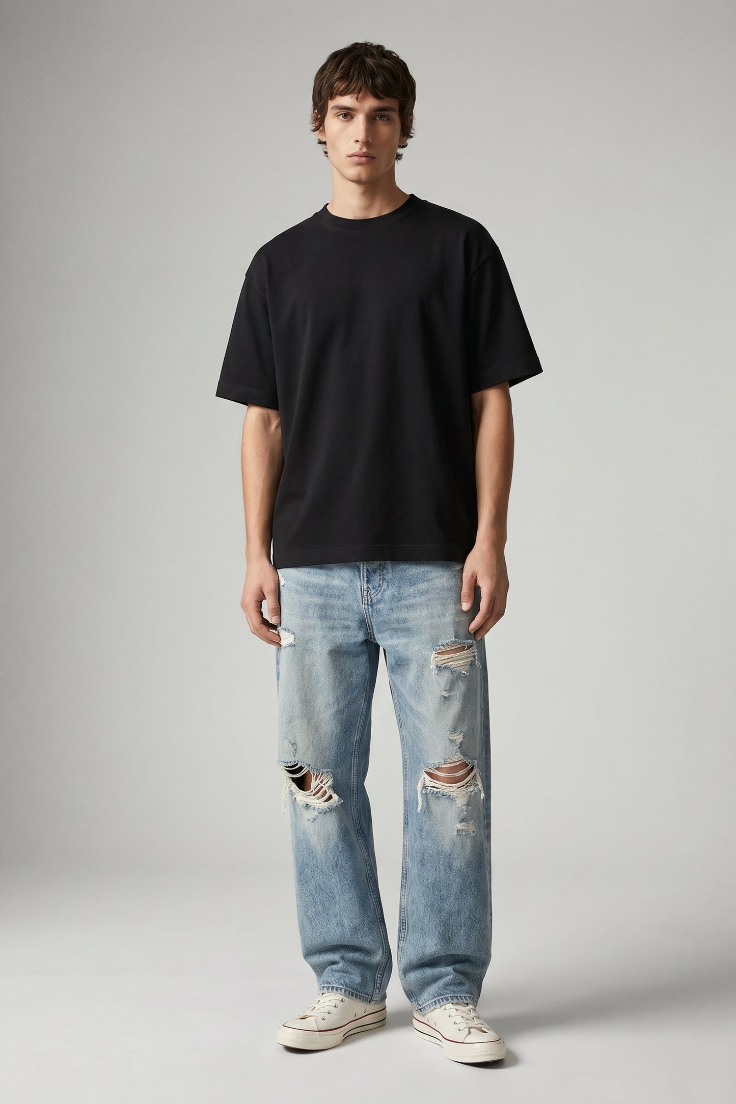 Person wearing a black t-shirt and light blue ripped jeans on a gray background