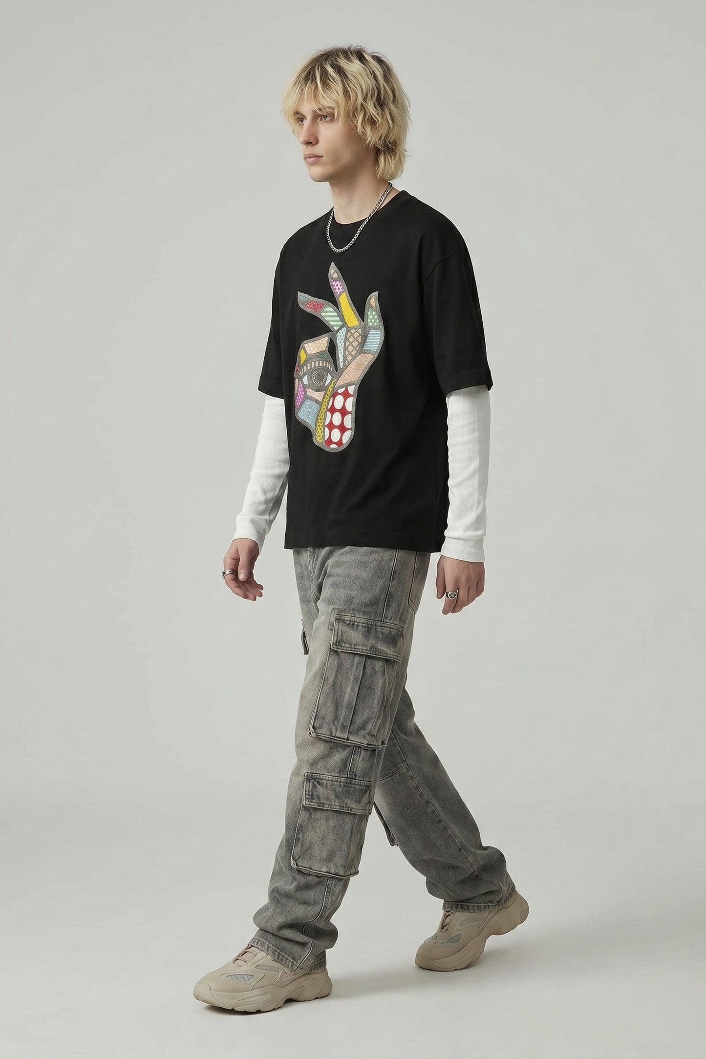 Person wearing a black graphic t-shirt, light gray cargo pants, and beige shoes on a plain background