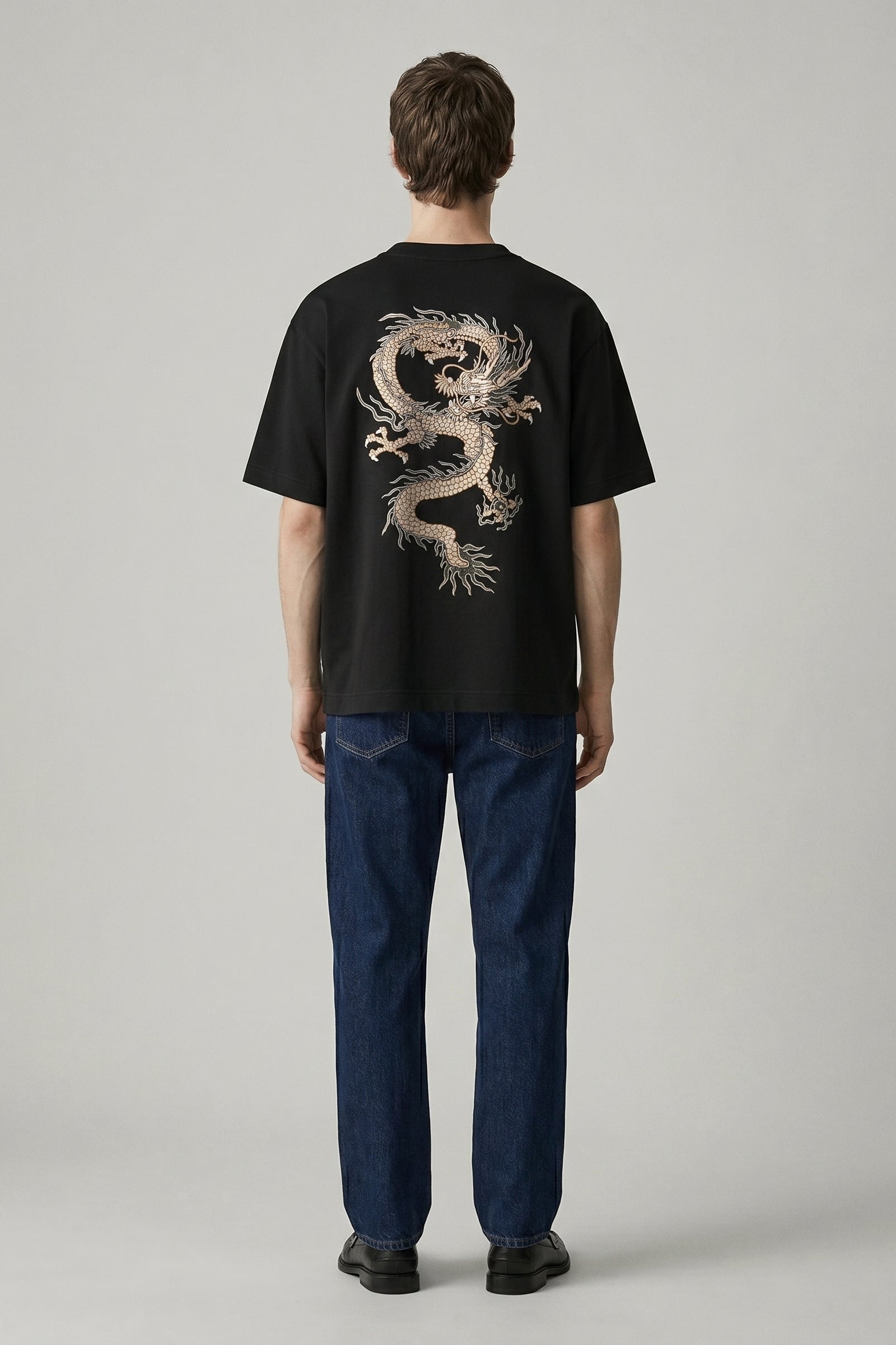 Person wearing a black t-shirt with a dragon design on the back, standing against a plain background.