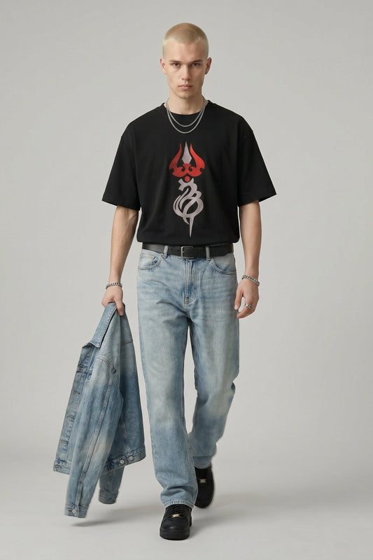 Man wearing a black t-shirt with a logo and light blue jeans, holding a denim jacket.