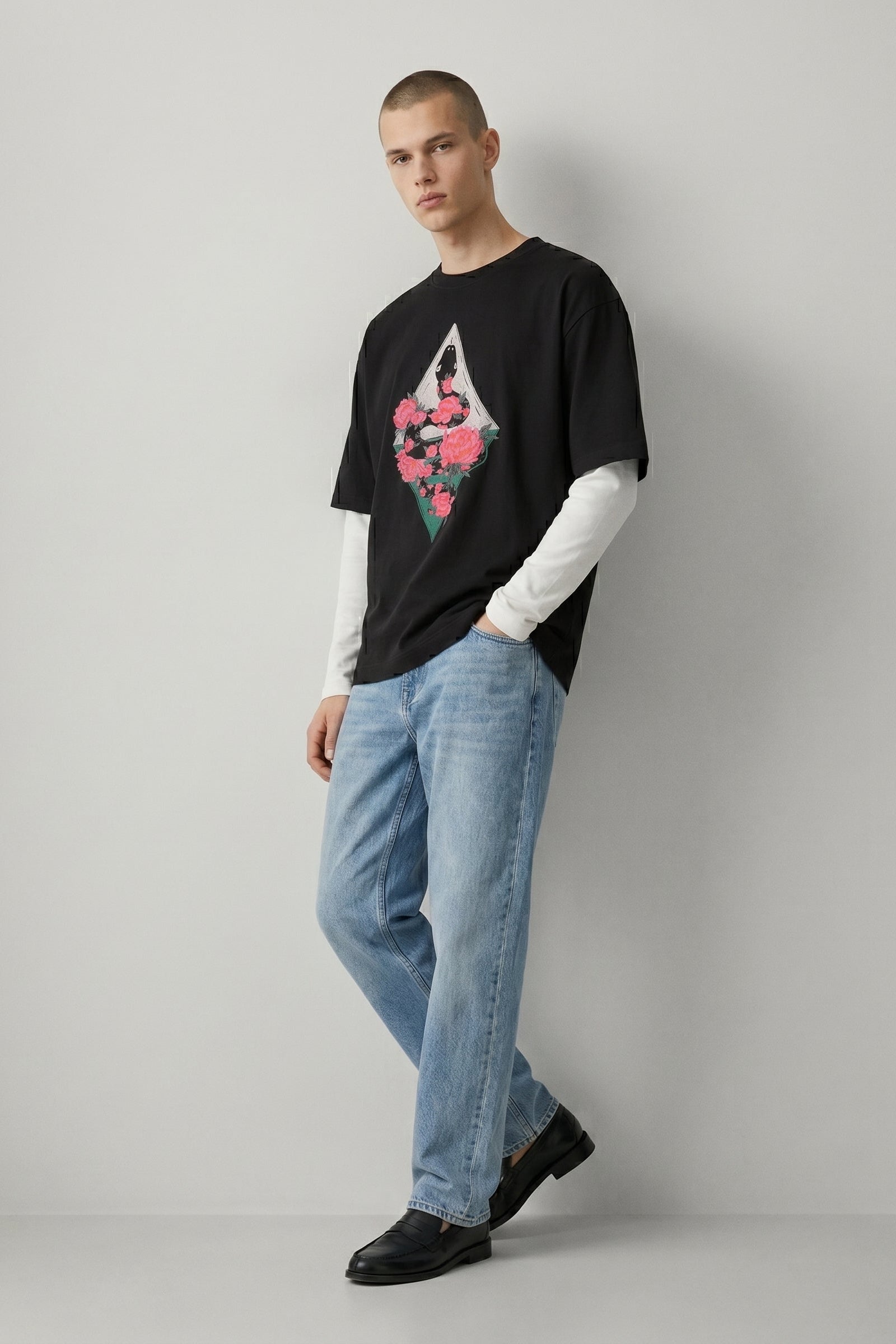 Person wearing a black t-shirt with a graphic design and light blue jeans on a plain background