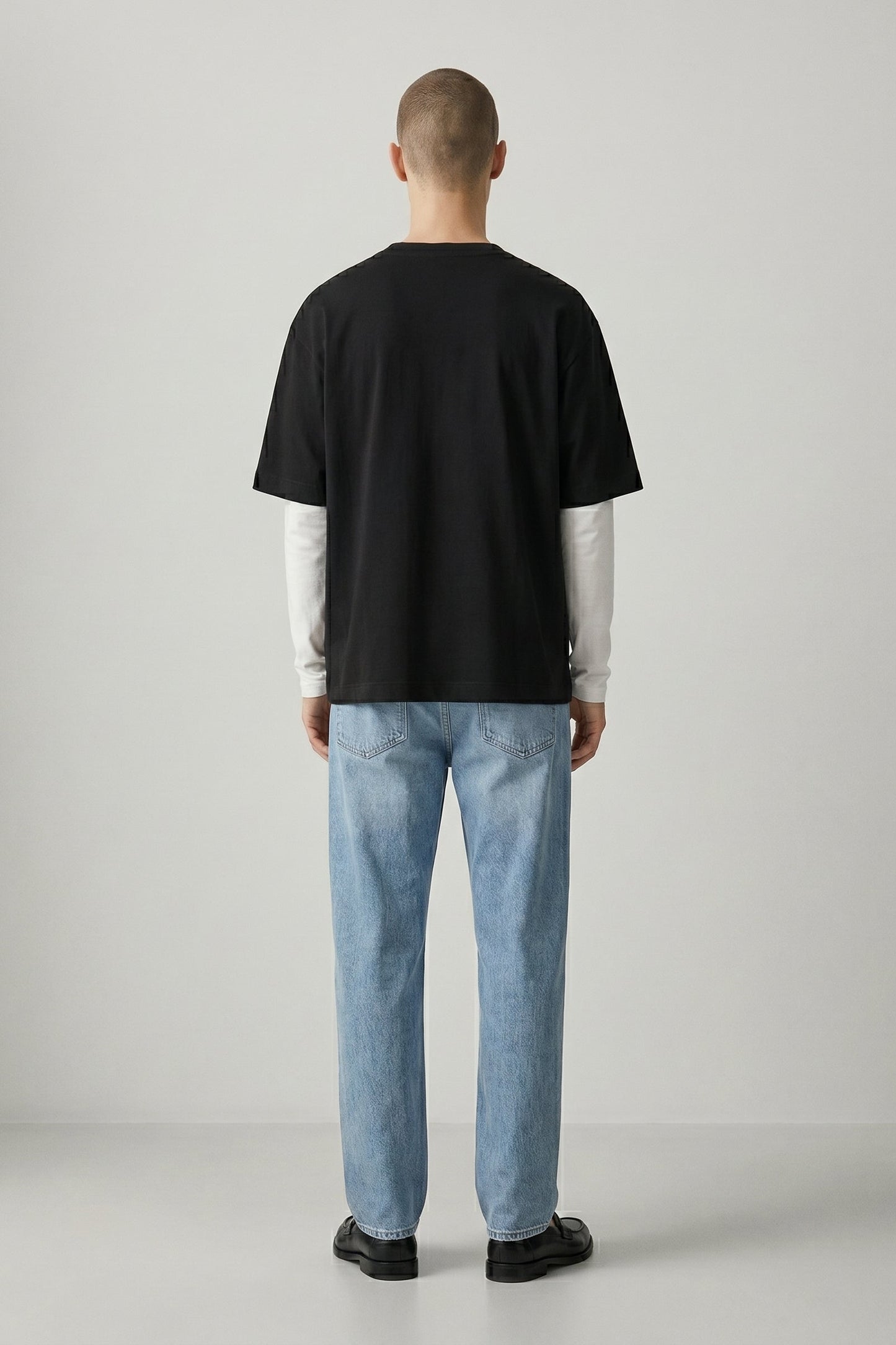 Person wearing a black t-shirt and light blue jeans standing against a plain background