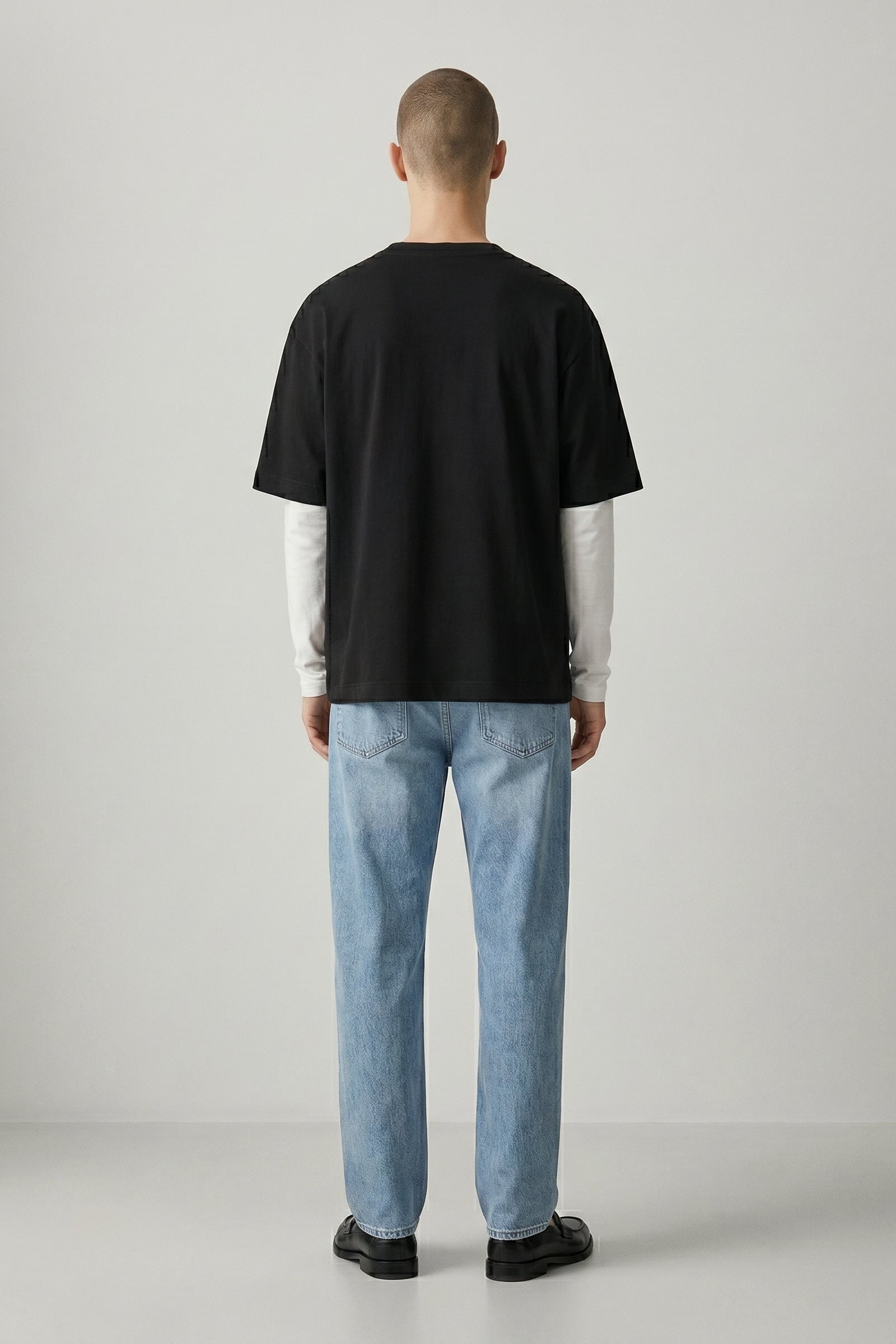 Person wearing a black t-shirt and light blue jeans standing against a plain background