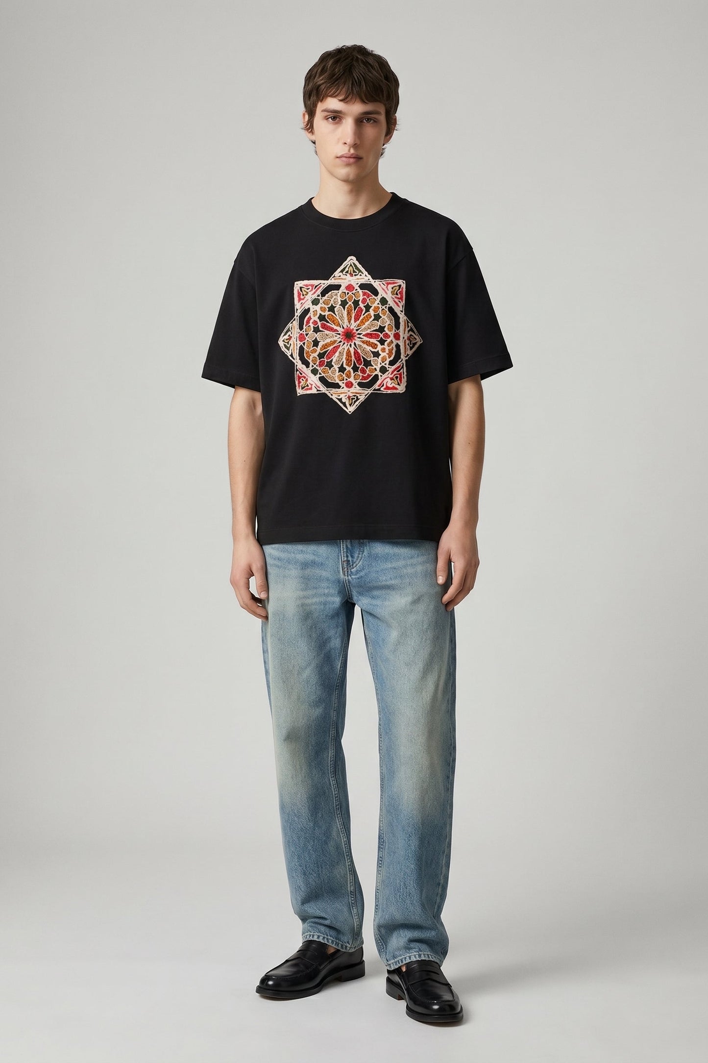 Person wearing a black t-shirt with a colorful geometric design and blue jeans on a gray background