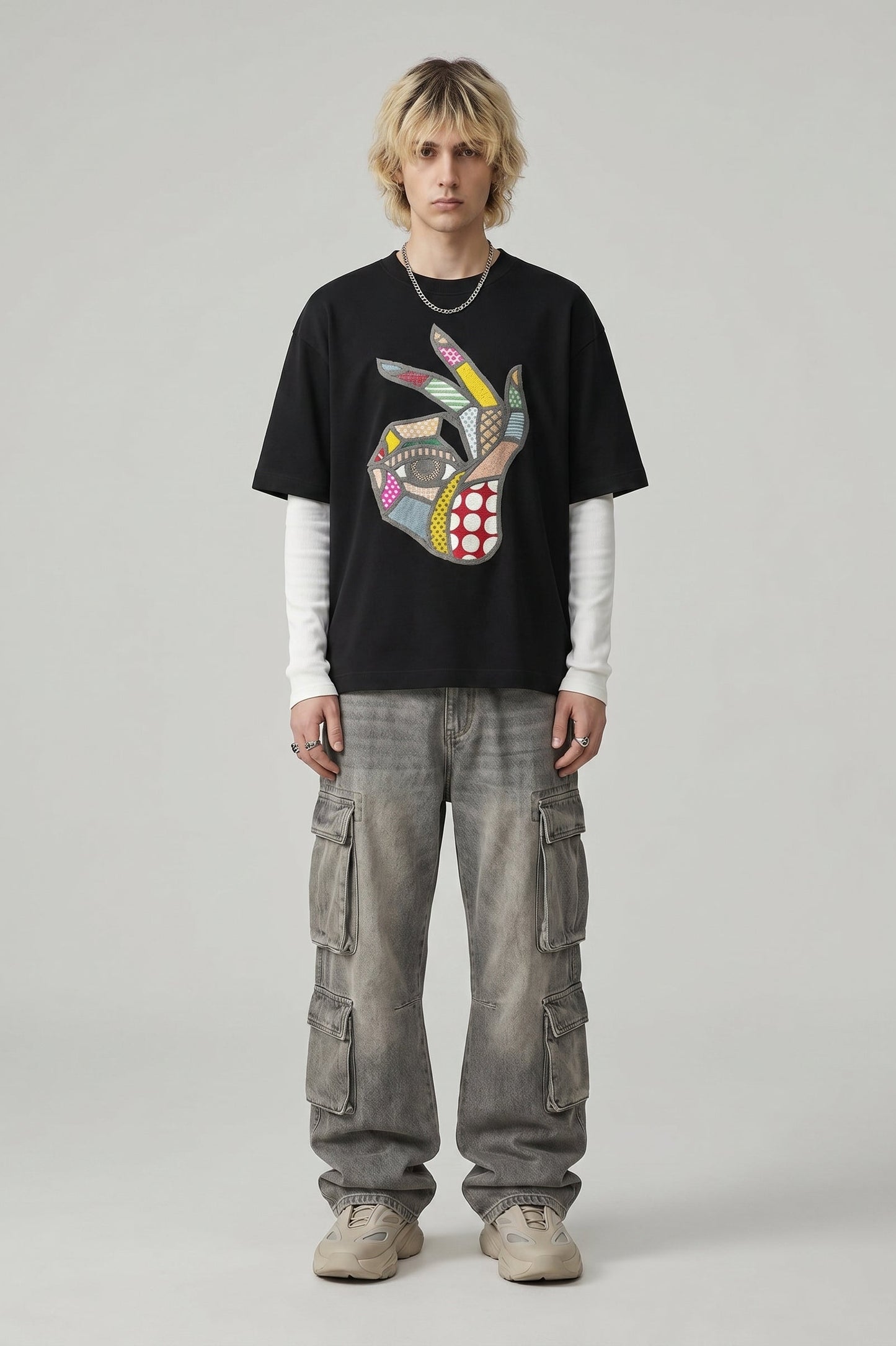 Person wearing a black t-shirt with a colorful graphic design and gray cargo pants on a plain background