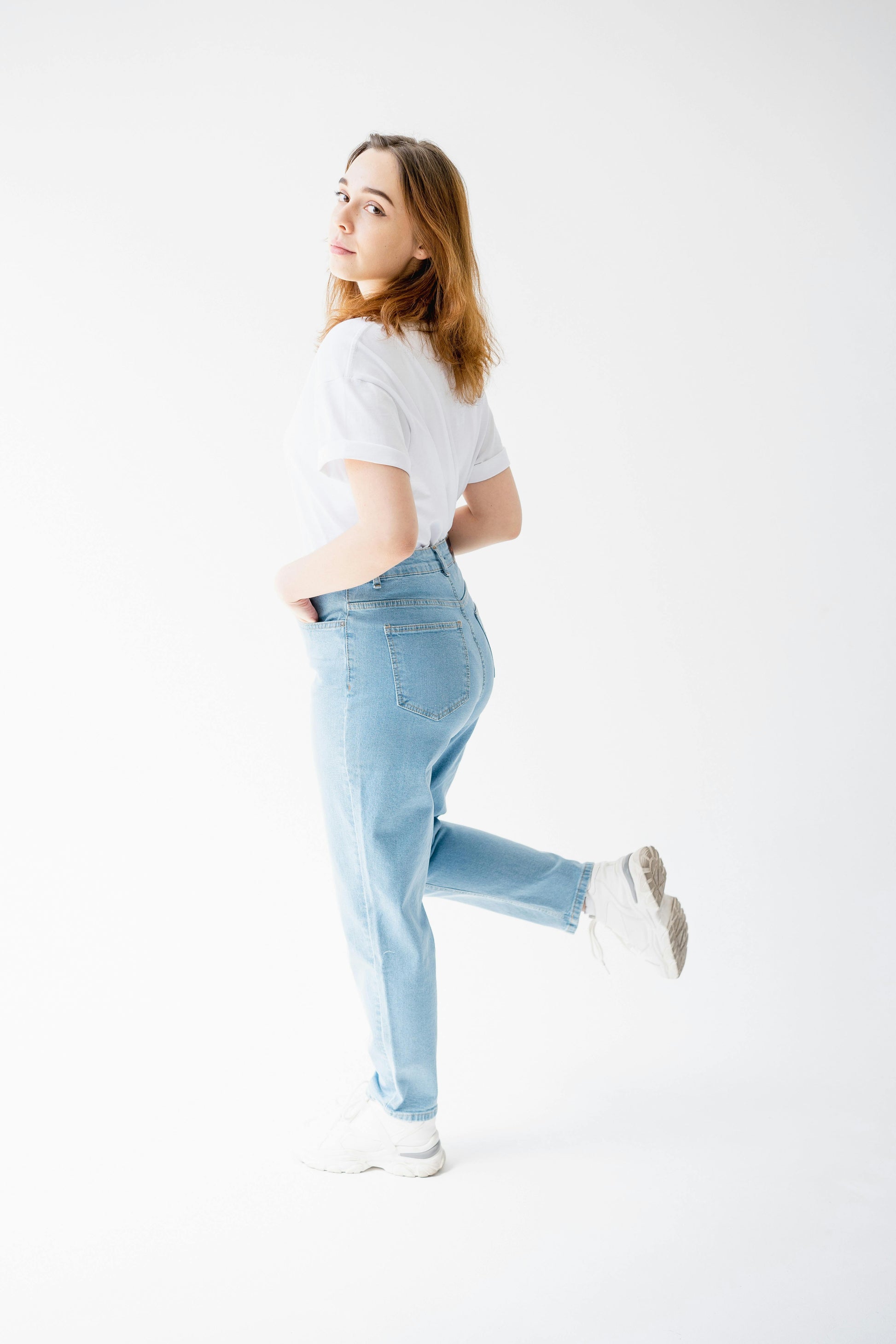 Woman wearing light blue jeans and a white t-shirt on a white background