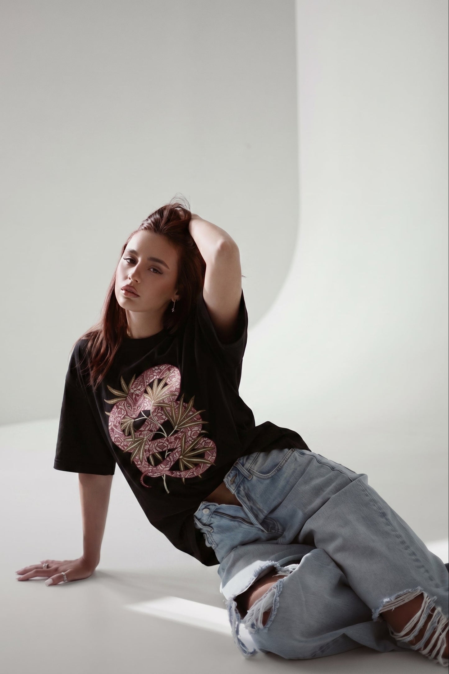 Person wearing a black t-shirt with a pink graphic design and light blue jeans on a white background