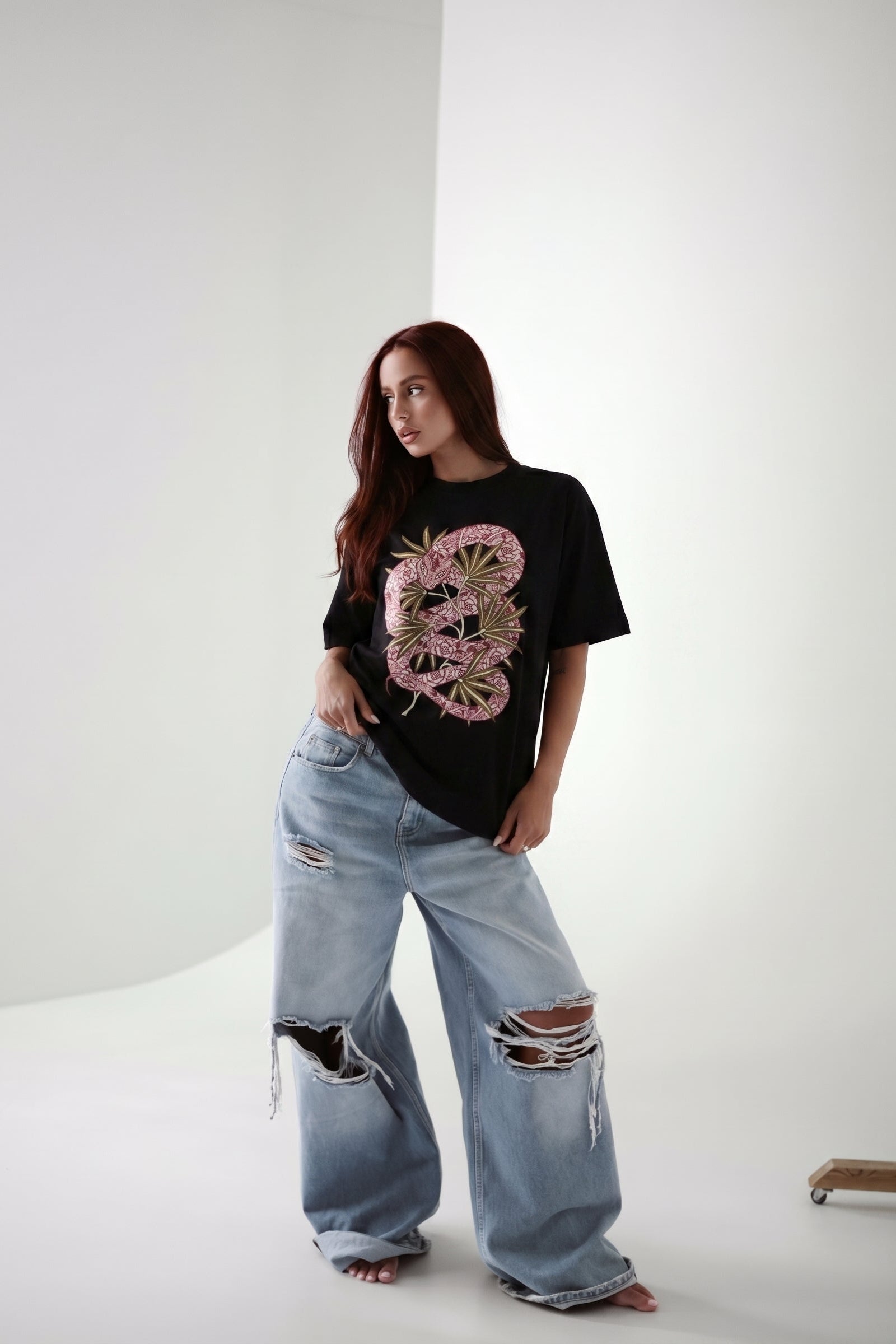Person wearing a black t-shirt with a pink floral design and light blue jeans on a white background