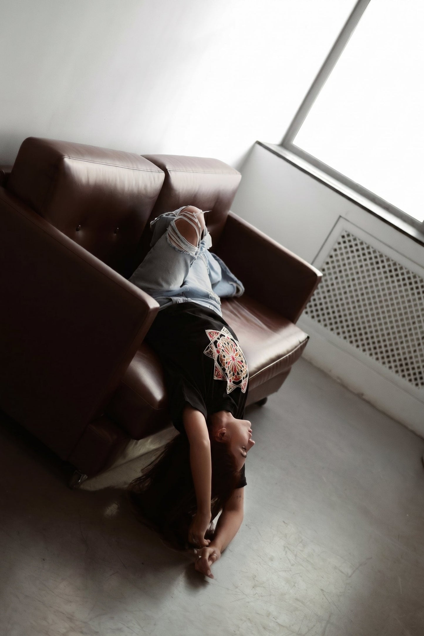 Person lying on a brown couch in a room with a window.