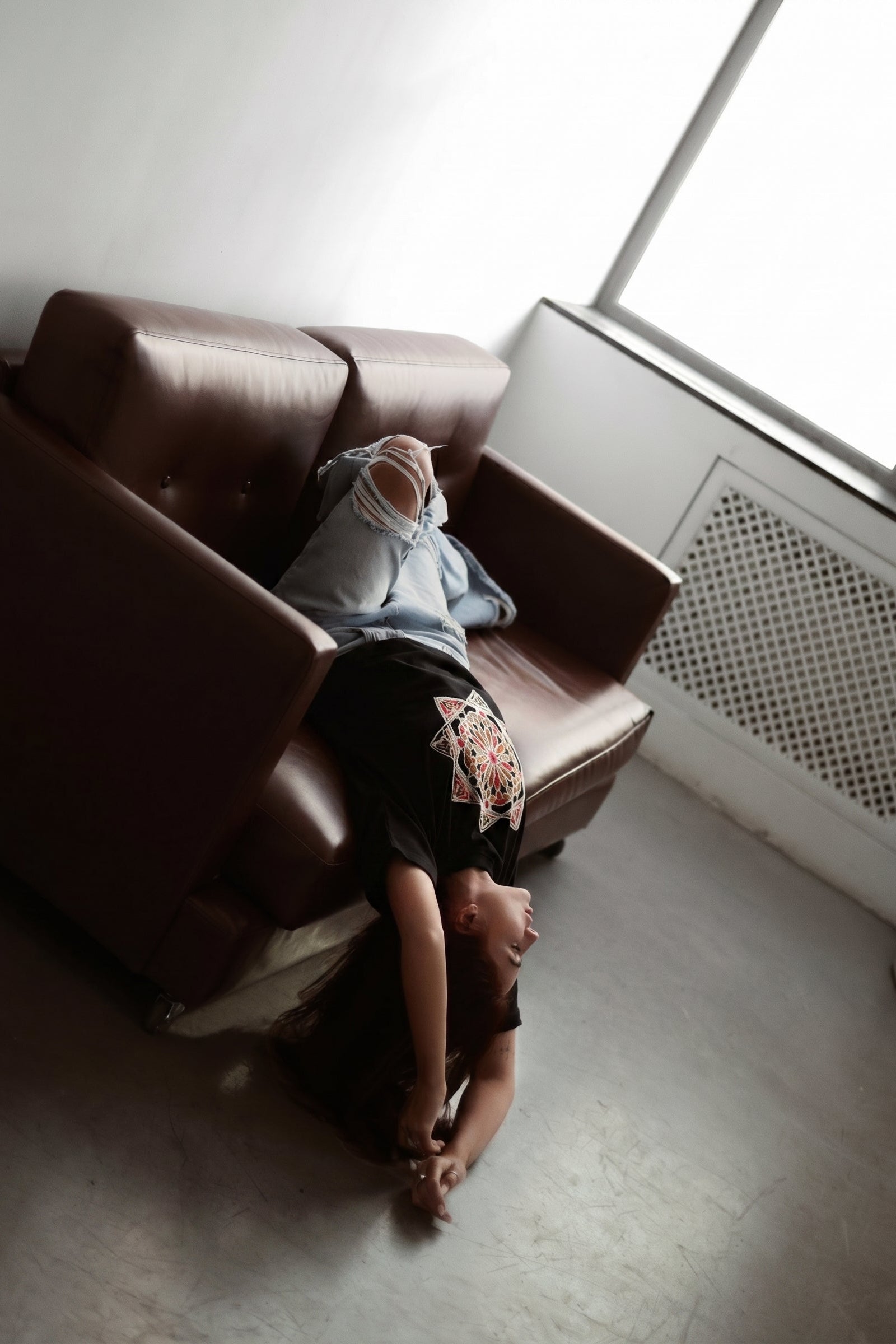 Person lying on a brown couch in a room with a window.