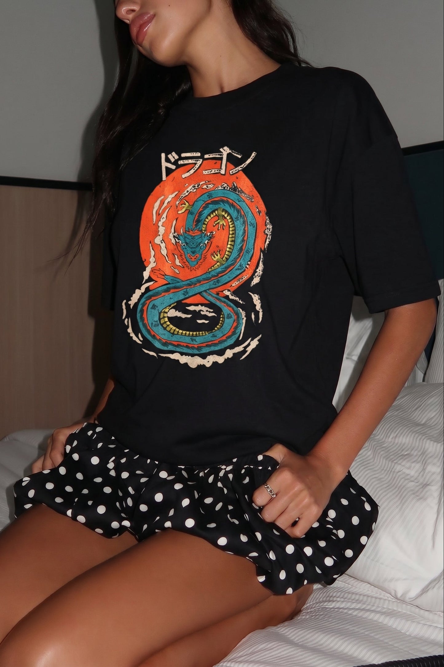 Person wearing a black t-shirt with a colorful dragon design and a polka dot skirt.