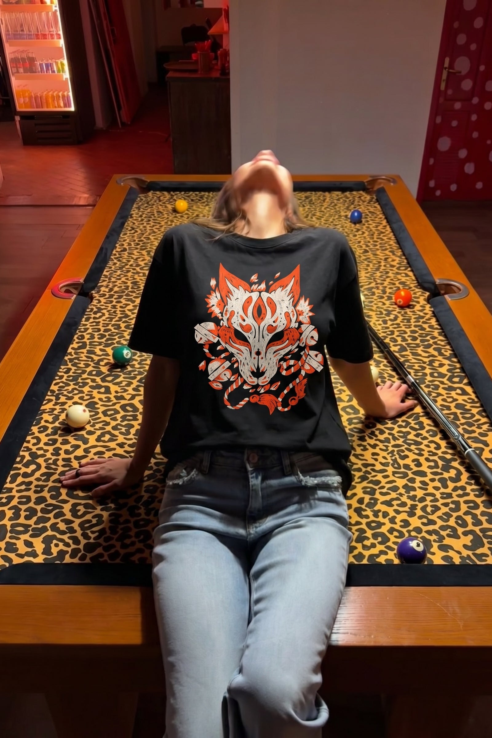 Person wearing a black t-shirt with a red and white design on a pool table.