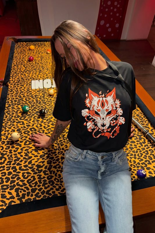 Person wearing a black t-shirt with a fox design in front of a pool table with a leopard print felt.